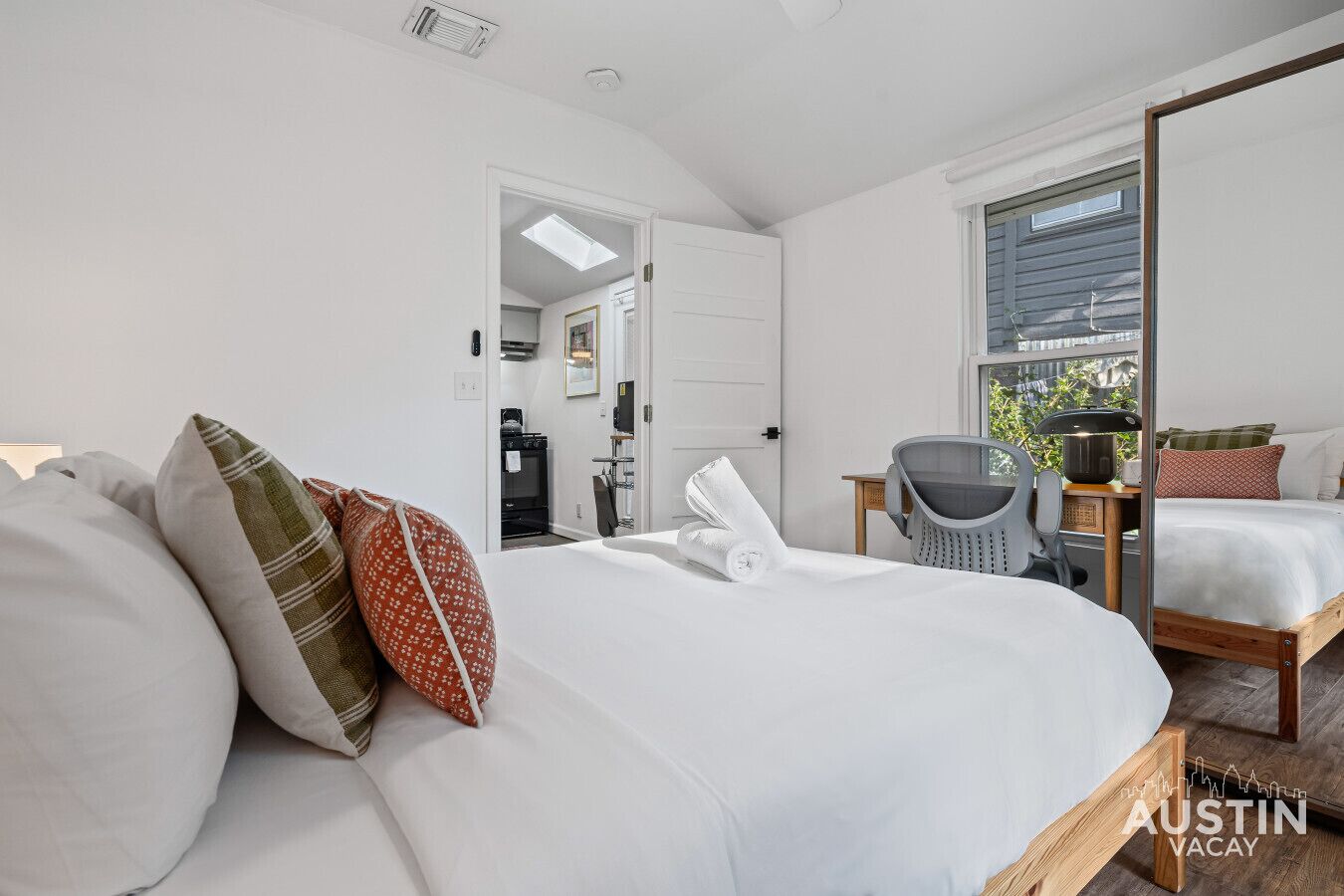 A modern bedroom with a large bed, a mirror, a small table, and a view of the outdoors.