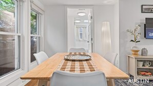 Un comedor con una mesa de madera, sillas blancas y un mantel a cuadros.