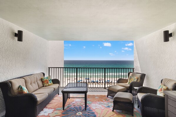 A balcony with wicker furniture, a patterned rug, and a view of the ocean.