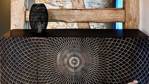 A rustic interior with exposed wooden beams, a black geometric-patterned shelf, and a stone wall.