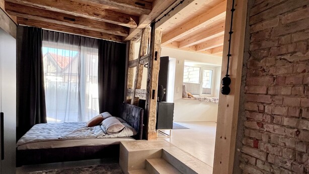A bedroom with a bed, a small table, a TV, and a window with curtains.