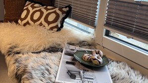 A cozy seating area with a fur rug, a window with blinds, and a plate of pastries on a magazine.