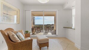 Una habitación con una silla de mimbre, un reposapiés y vistas a un balcón con mobiliario exterior.