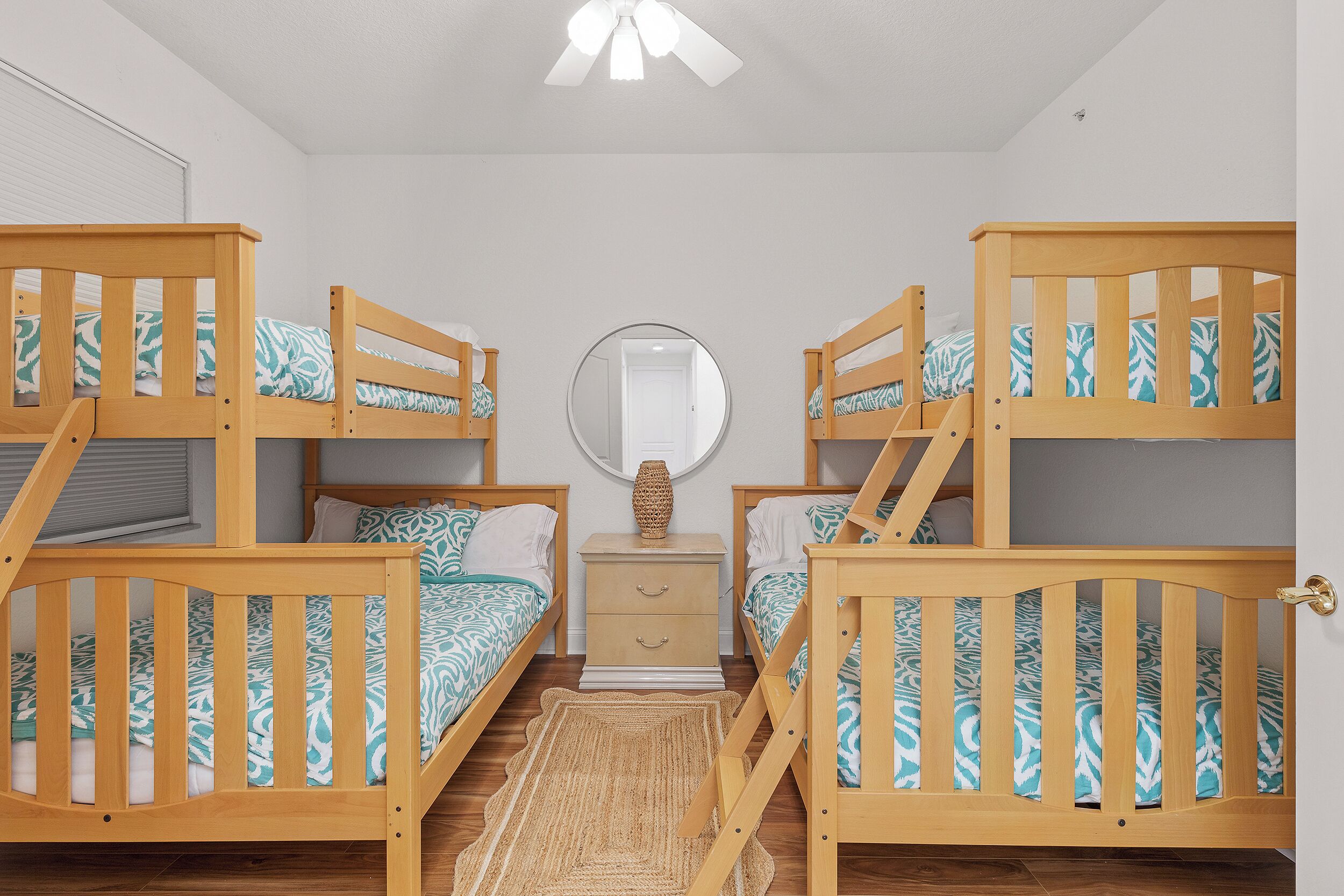 A room with two bunk beds, a bedside table with a lamp, a mirror, and a small rug.
