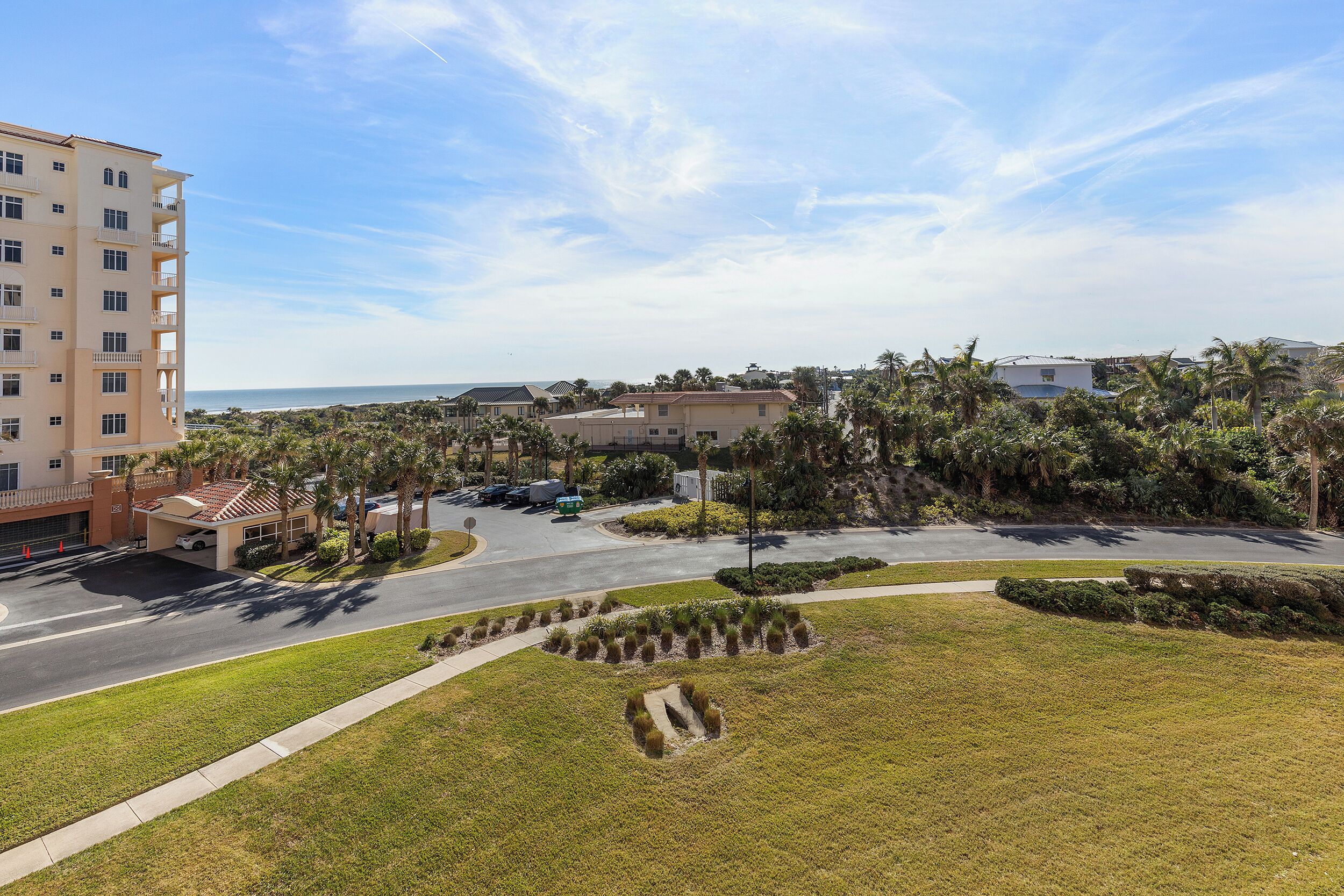 A hotel with a parking area, a road, and a view of the ocean.