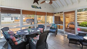 Un patio couvert aménagé avec des meubles en osier, un ventilateur de plafond et de grandes fenêtres offrant une vue sur l’extérieur.