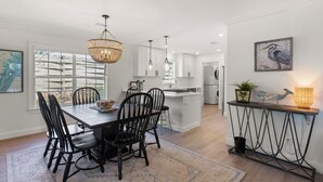 Une cuisine moderne avec des meubles blancs, un coin repas avec des chaises noires et une grande fenêtre qui laisse entrer la lumière naturelle.