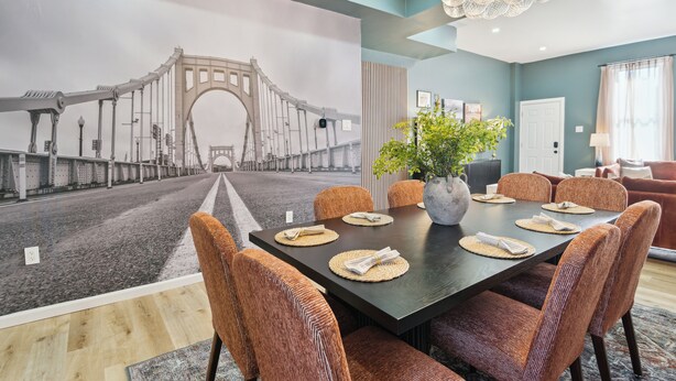 A dining area with a large table, wicker chairs, a vase with flowers, and a mural of a bridge on the wall. - 5 minutes to Stadium/Casino/PNC. Spacious house with WiFi, Game/Movie Rooms (Pittsburgh)