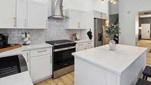 A modern kitchen with white cabinetry, a stainless steel range hood, a built-in oven, and a central island with a vase of green plants. - 5 minutes to Stadium/Casino/PNC. Spacious house with WiFi, Game/Movie Rooms (Pittsburgh)