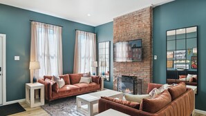 A living room with a brick fireplace, two sofas, a coffee table, and a TV mounted on the wall. - 5 minutes to Stadium/Casino/PNC. Spacious house with WiFi, Game/Movie Rooms (Pittsburgh)