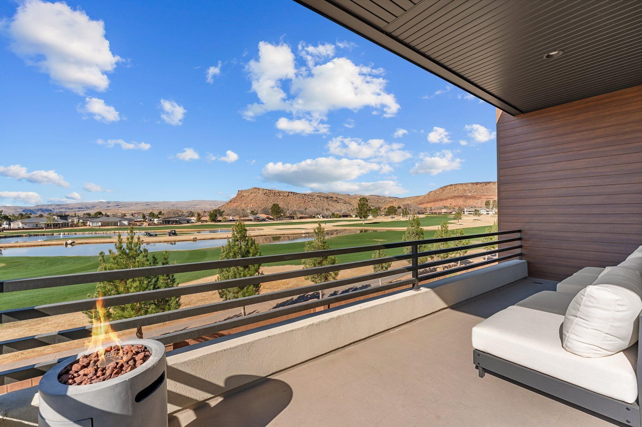 Un balcon avec un foyer extérieur, un canapé blanc et une vue sur un terrain de golf et des montagnes.