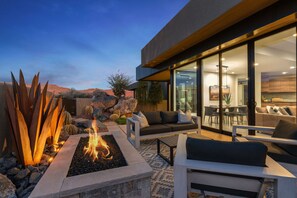A modern outdoor living area with a fire pit, seating, and a view of the interior. - Serene Views:  Luxurious 3 bedroom home, Community Pool, Stunning Views! (Ivins)