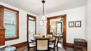 A dining room with a round table, chairs, a chandelier, wooden floors, and a rug.
