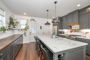 A modern kitchen with a large island, dark cabinets, and pendant lighting.