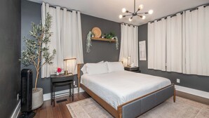 Un dormitorio moderno con una cama grande, mesitas de noche, una lámpara de pie, un estante en la pared con plantas y una lámpara de techo.