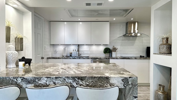 Une cuisine moderne avec des meubles blancs, un plan de travail en granit et un îlot central doté de tabourets de bar.