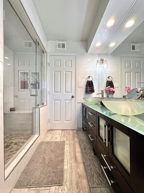 A modern bathroom with a glass shower enclosure, a large mirror, and a vanity with a glass countertop. - Perfect for Every Adventurer! Visit for venues and views (Phoenix)