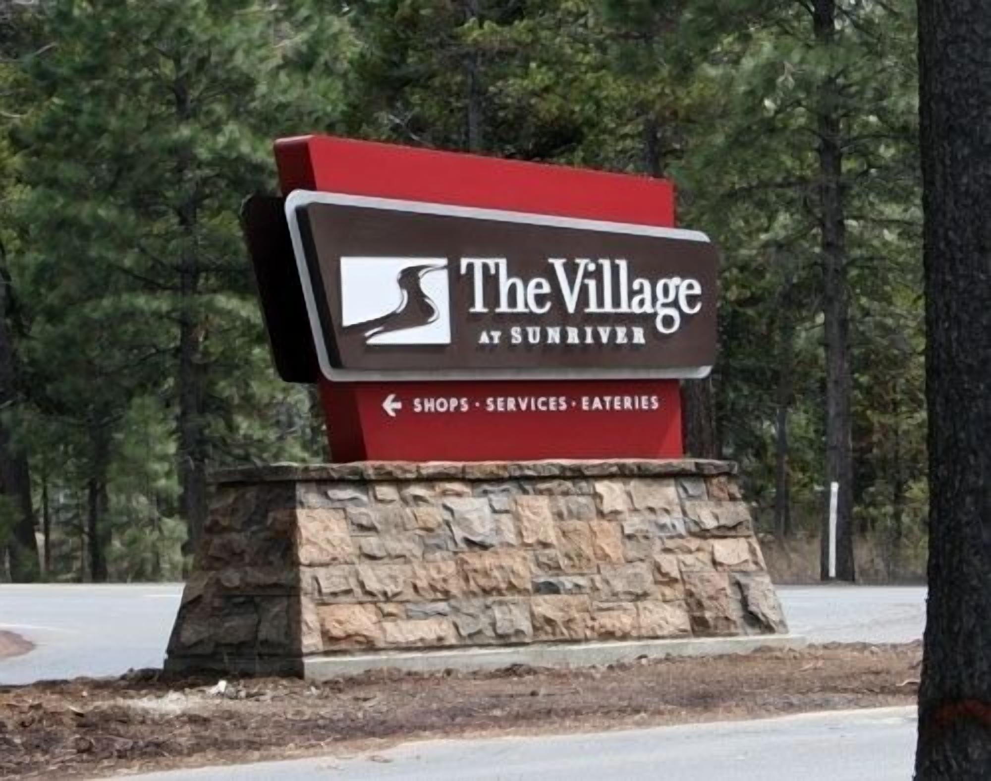 A sign for 'The Village at Sunriver' with a logo and directional arrow pointing left for shops, services, and eateries.
