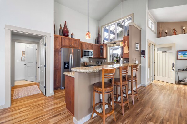 Una cocina con armarios de madera, una isla central con taburetes de bar, un microondas y un refrigerador.