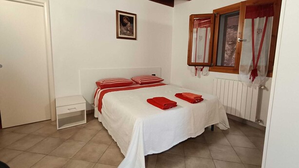 A bedroom with a bed, a nightstand, a window with curtains, and a radiator. - Studio apartment "Zone" (Lombardia)