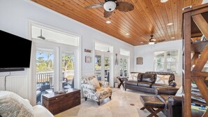 A spacious living room with a wooden ceiling, a large sofa, a coffee table, and a television mounted on the wall. - Foosball | Hot Tub | LSV | Pool Access (Port St Joe)