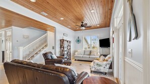 A spacious living room with a wooden ceiling, a staircase, a leather sofa, a white sofa, and a round wooden table. - Foosball | Hot Tub | LSV | Pool Access (Port St Joe)