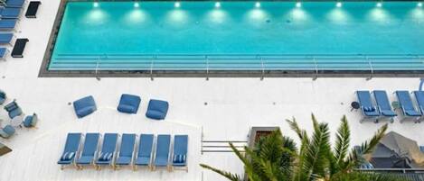 A large indoor swimming pool with blue lounge chairs and sun loungers arranged around it.