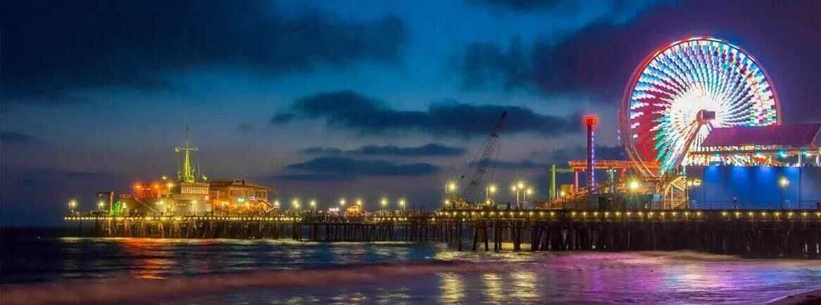 A pier with a large Ferris wheel and a building with lights.