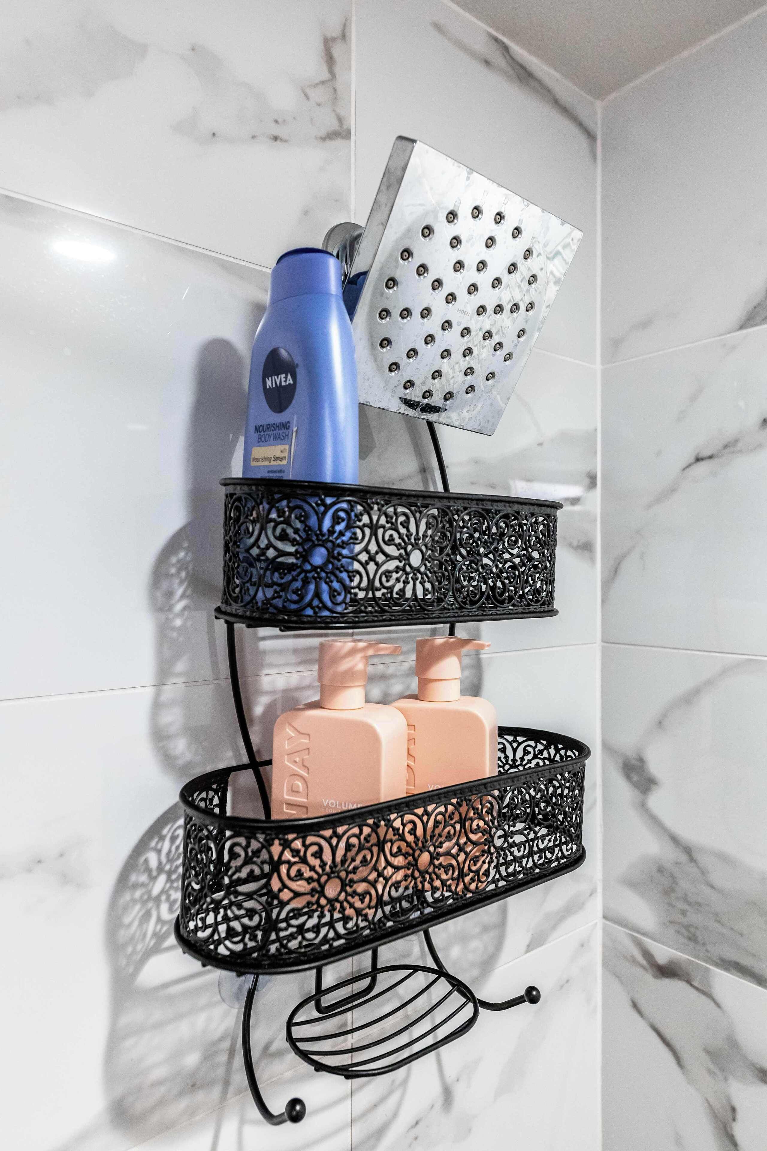 A bathroom with a marble wall, a black metal shelf holding toiletries, and a shower head.