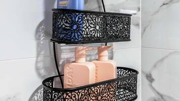 A bathroom with a marble wall, a black metal shelf holding toiletries, and a shower head.