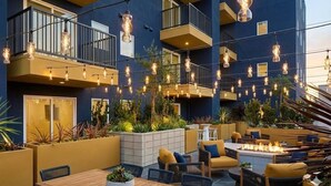 Un espace extérieur aménagé en terrasse, avec des sièges et un foyer, entouré de jardinières et de luminaires suspendus.