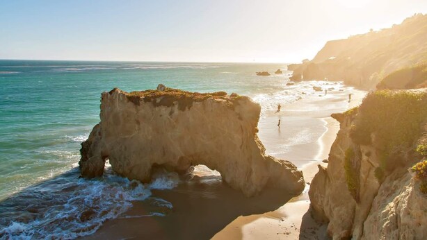 Un paysage côtier caractérisé par une formation rocheuse imposante et une plage.