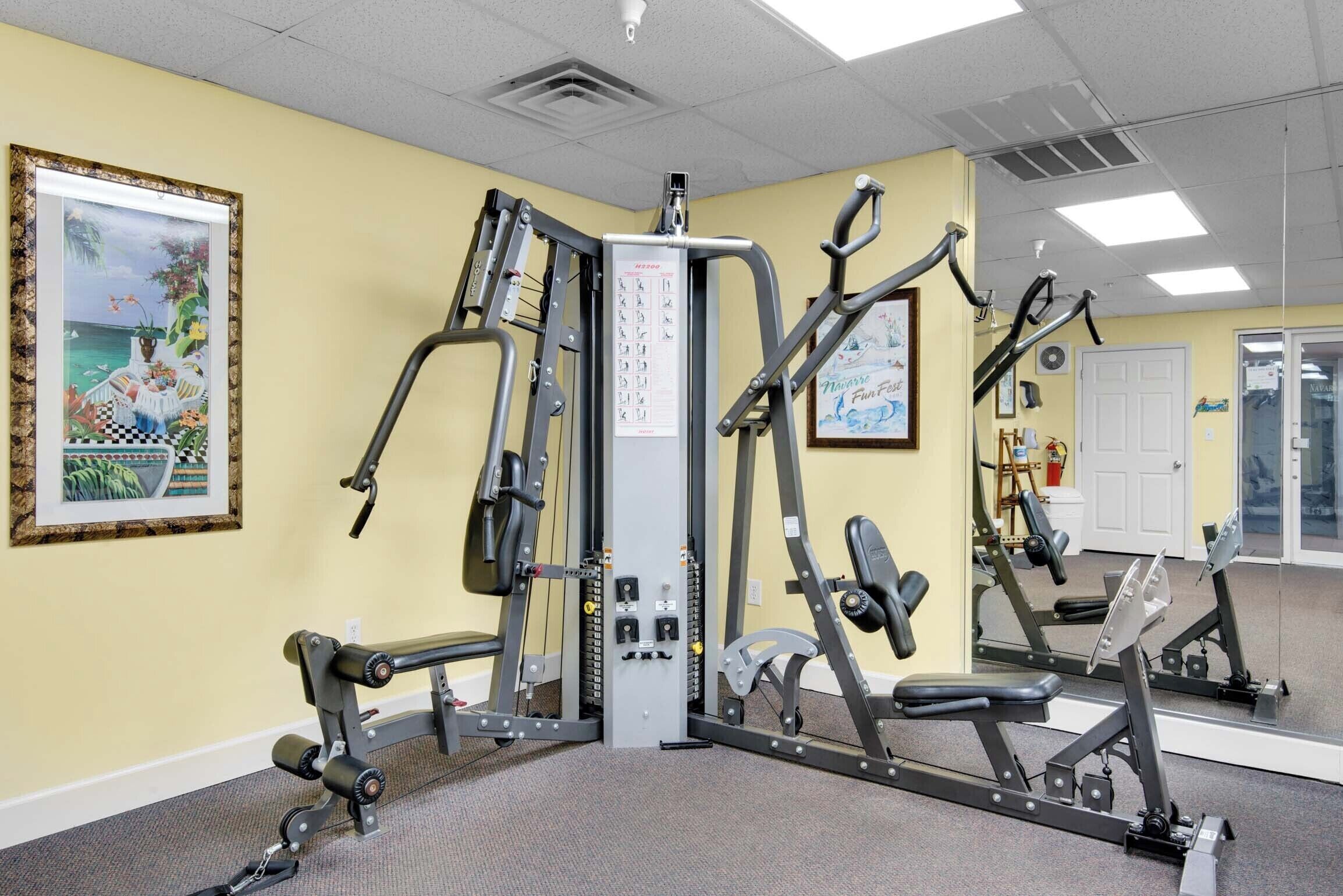 Une salle de sport équipée de matériel d’exercice, avec un miroir et un tableau encadré accroché au mur.