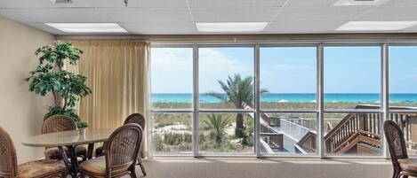 A conference room with a large table and chairs, a potted plant, and a view of the beach through large windows.