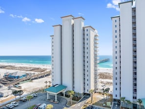 A high-rise hotel with a beach view, multiple balconies, and a parking area.