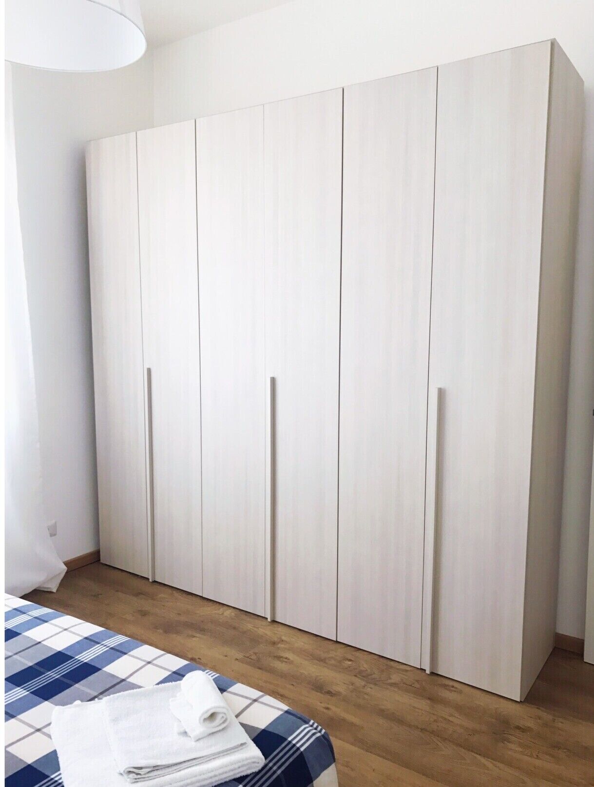 Une chambre avec une grande armoire, un lit recouvert d’une couette à carreaux bleus et blancs, et un plancher en bois.