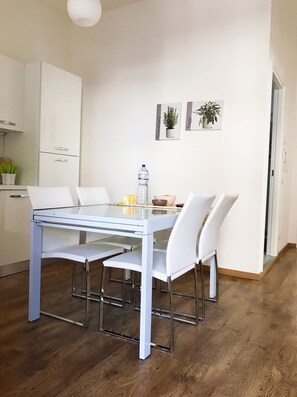A modern dining area with a glass table and white chairs, a water bottle, and a bowl on the table. - BLUE HOUSE (Porto Sant'Elpidio)