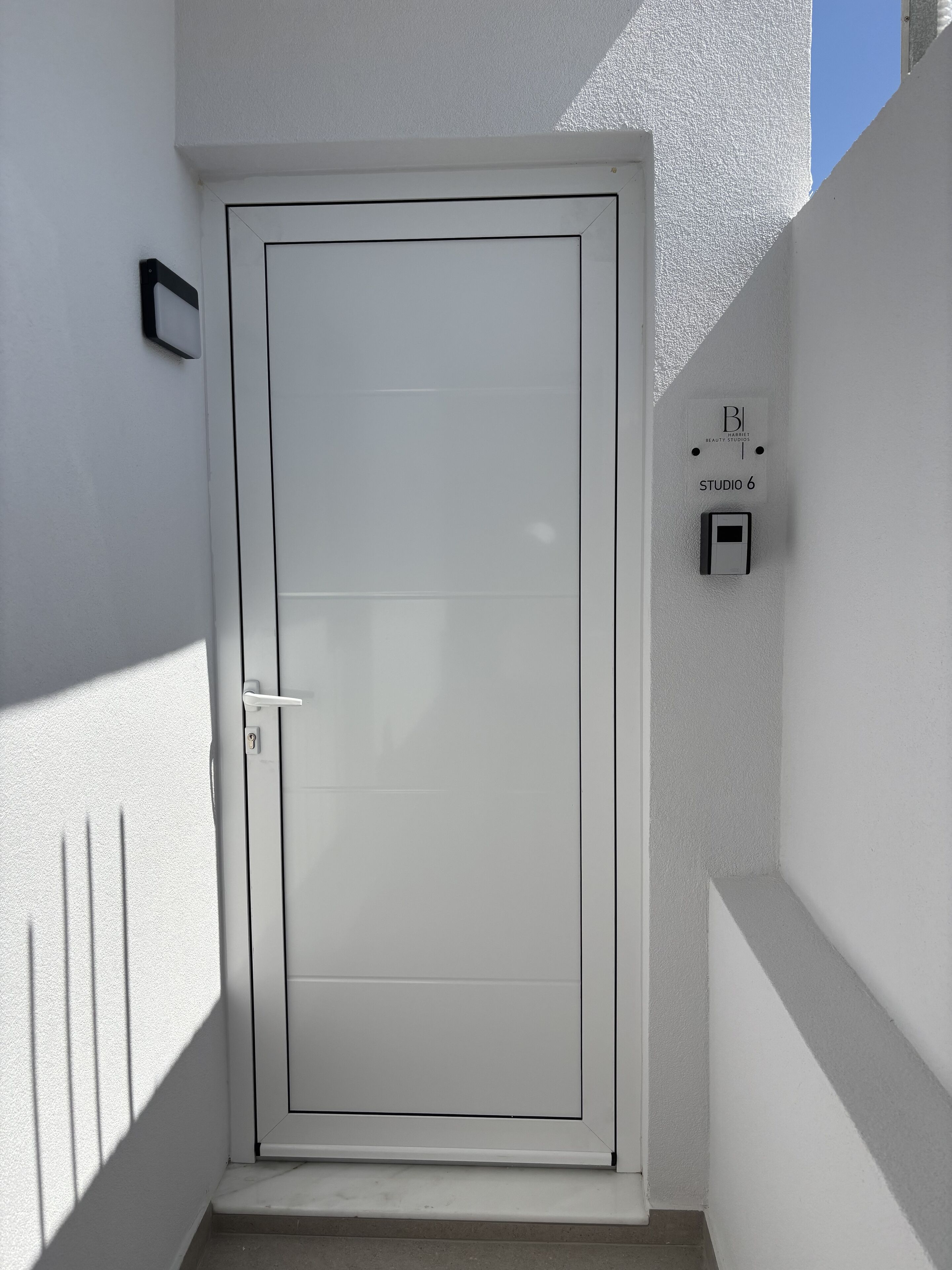 Una puerta blanca con una cerradura y un pomo, un pequeño letrero encima, y una sombra en la pared.