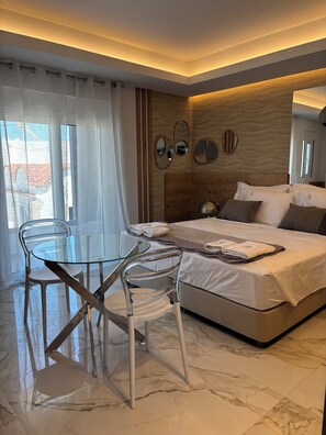 Una habitación de hotel moderna con una cama, una mesa de vidrio con sillas y vistas al exterior.