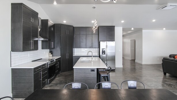 A modern kitchen with dark cabinetry, a central island, and a dining area with a dark wooden table and chairs. - Desert Dreams Retreat – Your Perfect Desert Getaway (3 Bedroom home & A Studio) (Moab)