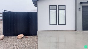 Un edificio moderno con facciata bianca, due finestre con cornici nere e una recinzione ondulata nera in primo piano.