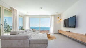Una sala de estar moderna con un amplio sofá modular, un televisor montado en la pared y vistas al mar a través de grandes ventanales.