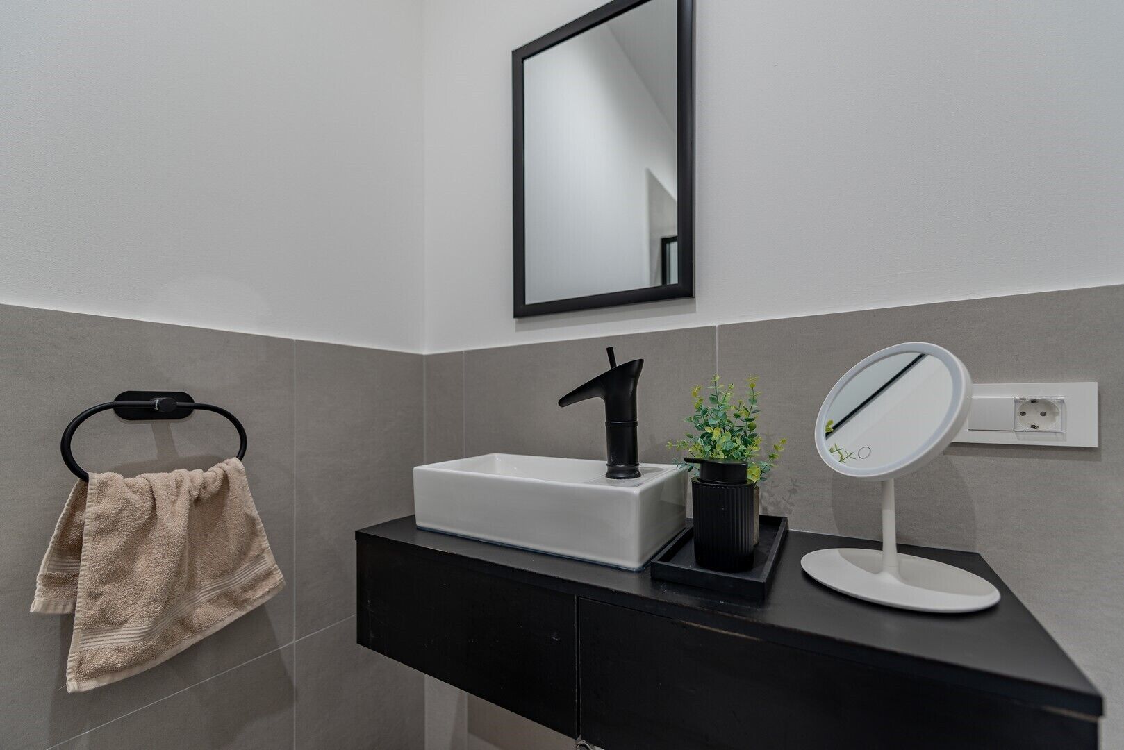 A modern bathroom with a black sink, a mirror, and a towel rack.