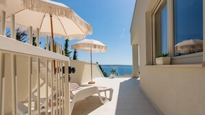 Un espacio de estar al aire libre iluminado por el sol, con sillones blancos y sombrillas, con vista a un mar azul y despejado.