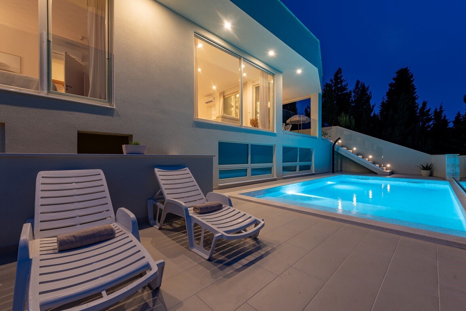 Una casa moderna con piscina, dos sillones de descanso y una escalera que lleva al piso superior.