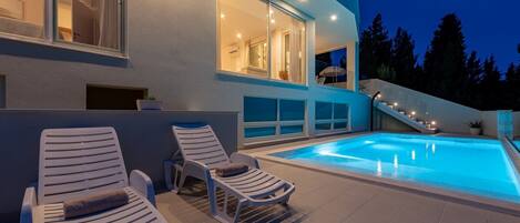 Una casa moderna con piscina, dos sillones de descanso y una escalera que lleva al piso superior.