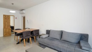 A modern living room with a grey sofa, a wooden dining table with four chairs, and a small grey side table.