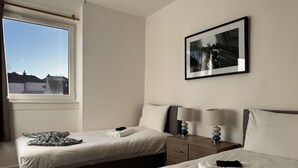 Una habitación de hotel con dos camas, una mesita de noche, una lámpara y un cuadro en la pared.