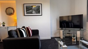Una sala de estar moderna con un sofá, un televisor de pantalla plana, una mesa de centro y un cuadro abstracto enmarcado en la pared.