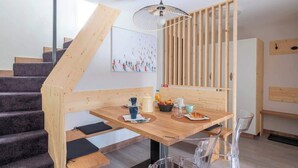 Una cocina moderna con detalles de madera, un comedor con una mesa y sillas de madera, y una escalera con peldaños de madera.